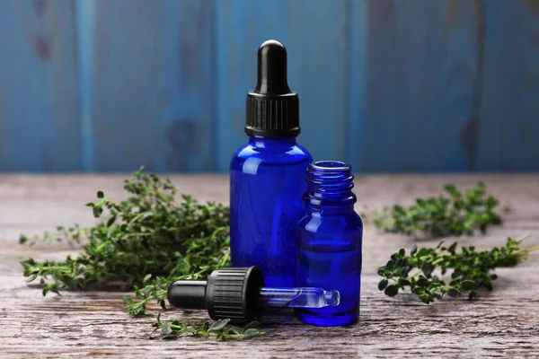 Bottles of thyme essential oil and fresh plant on wooden table