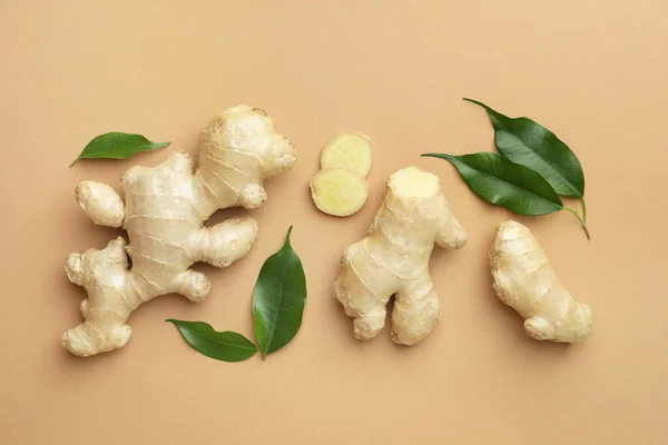Fresh ginger with green leaves on light pale brown background, flat lay