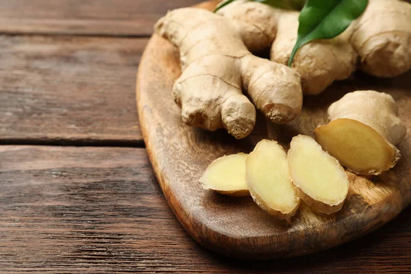 Cut and whole fresh ginger with leaves on wooden table, closeup. Space for text
