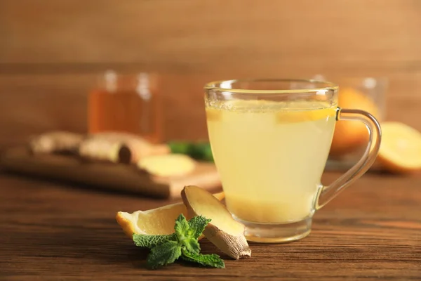 stock image Glass of aromatic ginger tea and ingredients on wooden table, closeup