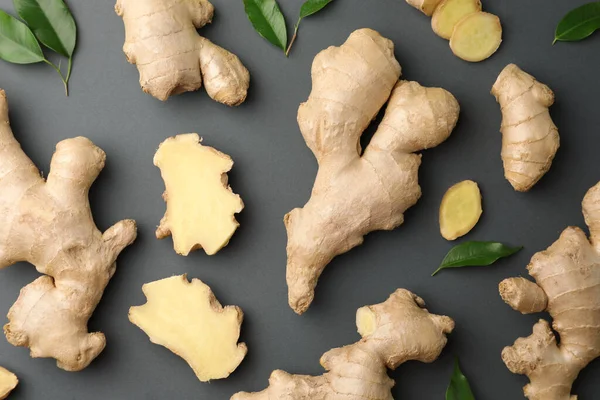 Fresh ginger with green leaves on dark background, flat lay