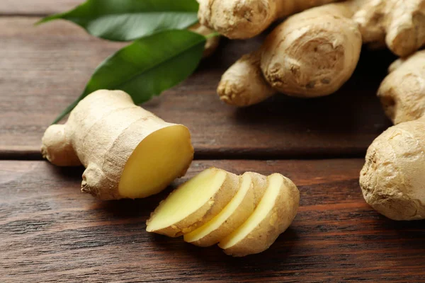 Cut and whole fresh ginger with leaves on wooden table, closeup