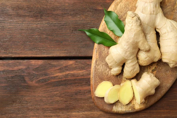 Cut and whole fresh ginger with leaves on wooden table, top view. Space for text
