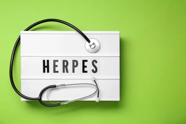 stock image Light box with word Herpes and stethoscope on green background, top view. Space for text