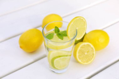 Bir bardak limonlu su ve beyaz ahşap masada nane.