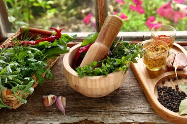 Kabuklu havan, taze yeşil otlar ve pencere kenarındaki ahşap masada farklı baharatlar.