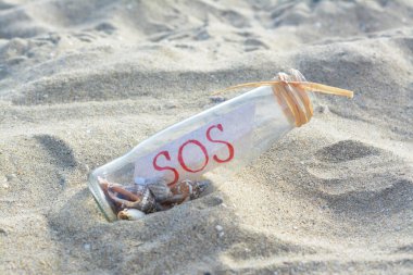 Deniz kabuklu cam şişe ve kumdaki SOS mesajı.