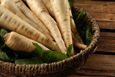 Fresh ripe parsnips in wicker basket on wooden table, closeup clipart