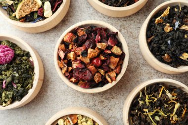 Açık gri masadaki ahşap kaselerde farklı türde kuru bitkisel çay.