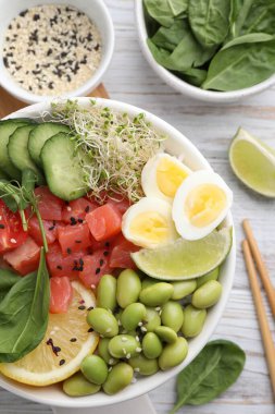 Beyaz ahşap masada bıldırcın yumurtalı, balıklı ve edamame fasulyeli nefis dürtme kasesi.