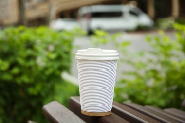 Paper cup of coffee on wooden bench outdoors. Takeaway drink