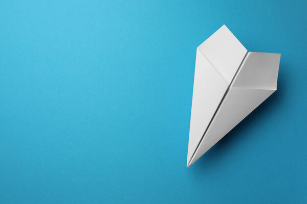 Handmade white paper plane on light blue background, top view. Space for text
