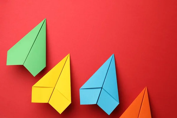Handmade colorful paper planes on red background, flat lay. Space for text