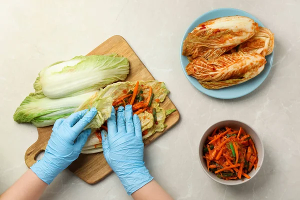 stock image Woman preparing spicy cabbage kimchi at beige marble table, top view