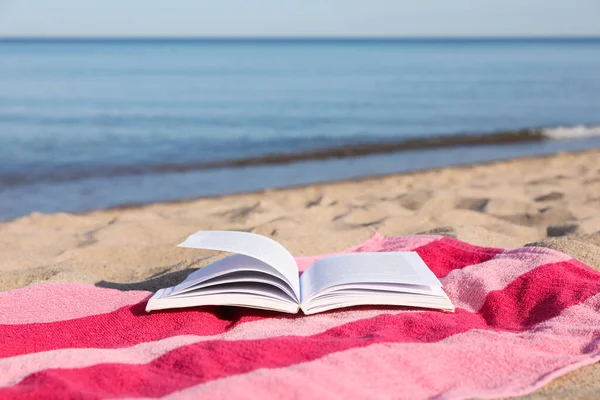 stock image Beach towel and open book on sand near sea, space for text