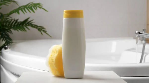 Bottle with foam bath and sponge on small table in bathroom
