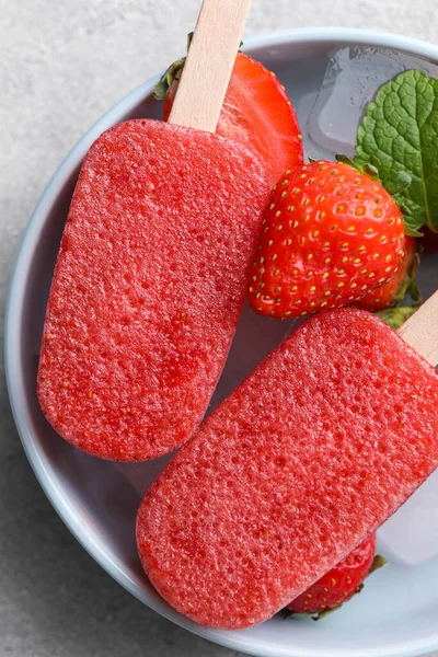 Bowl of tasty strawberry ice pops on grey table, top view. Fruit popsicle