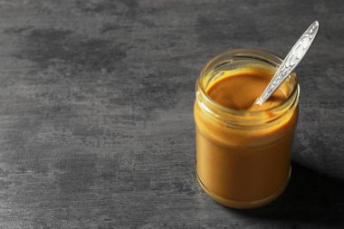 Koyu gri masada, cam kavanozda baharatlı hardal ve kaşık. Metin için boşluk