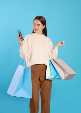 Alışveriş torbaları ve açık mavi arka planda akıllı telefonları olan mutlu genç bir kadın. Büyük indirim.