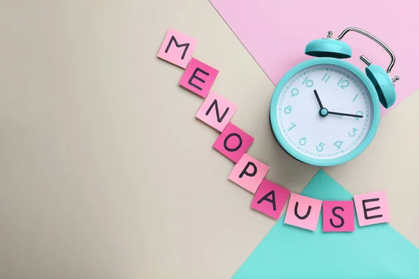 stock image Pink paper notes with word Menopause and alarm clock on color background, flat lay. Space for text