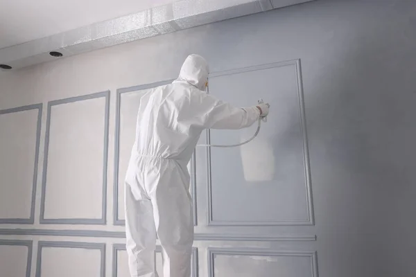 Decorator dyeing wall in grey color with spray paint