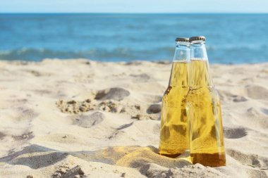 Bottles of cold beer on sandy beach near sea, space for text