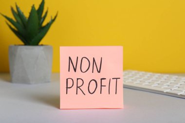 Kağıt notta Non Profit, klavye ve ev bitkisi beyaz masa üzerinde