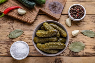 Bir kase salatalık turşusu ve ahşap masa üzerinde yiyecek koruma malzemesi.