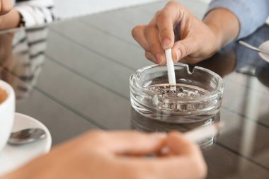 Masadaki kül tablasında sigara söndüren kadın, yakın plan.