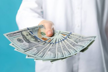 Turkuaz arka planda dolar banknotları tutan kadın, yakın plan. Para değişimi kavramı