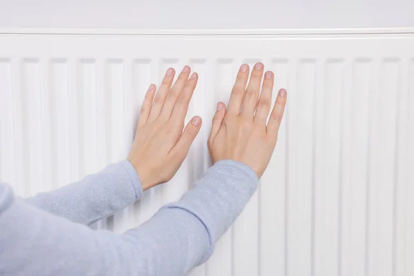 Woman warming hands on heating radiator, closeup