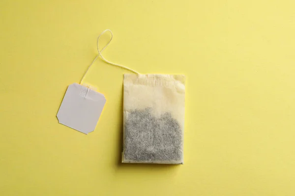 Paper tea bag with tag on yellow background, top view