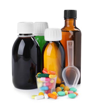 Şurup şişeleri, ölçü kabı, beyaz arka planda haplı plastik kaşık. Öksürük ve nezle ilacı