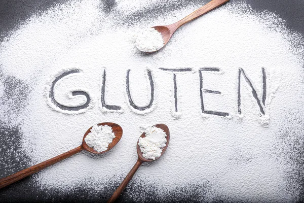 stock image Word Gluten made with flour and wooden spoons on grey background, flat lay