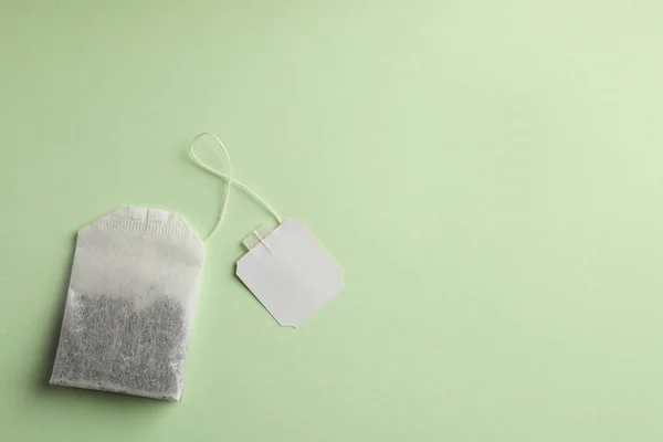 Paper tea bag with tag on light green background, top view. Space for text