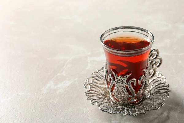 Glass of traditional Turkish tea in vintage holder on white marble table, closeup. Space for text