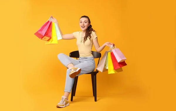 Szczęśliwa Kobieta Trzyma Kolorowe Torby Zakupy Krześle Pomarańczowym Tle — Zdjęcie stockowe