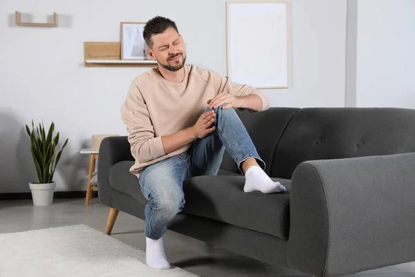 stock image Man suffering from knee pain on sofa at home