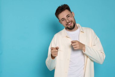 Beyaz ceketli yakışıklı adam açık mavi arkaplanı işaret ediyor, mesaj için yer var.