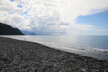 Güzel deniz kıyısı manzarası ve bulutlu gökyüzü altındaki dağlar.