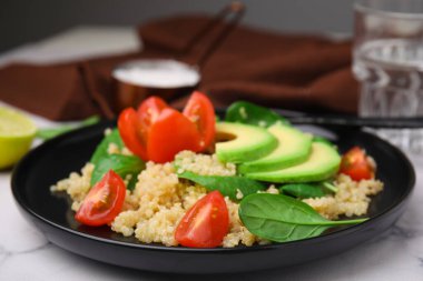 Domatesli nefis kinoa salatası, avokado dilimleri ve beyaz mermer masada servis edilen ıspanak yaprakları.