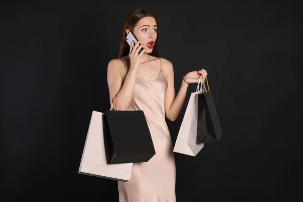 Überraschte Junge Frau Mit Einkaufstaschen Und Smartphone Auf Schwarzem Hintergrund — Stockfoto