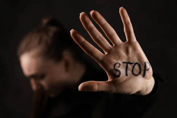 Woman with word Stop written on hand against dark background, closeup. Domestic violence concept