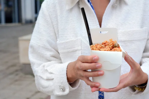 Stock image Woman holding paper box of takeaway noodles with fork outdoors, closeup. Street food