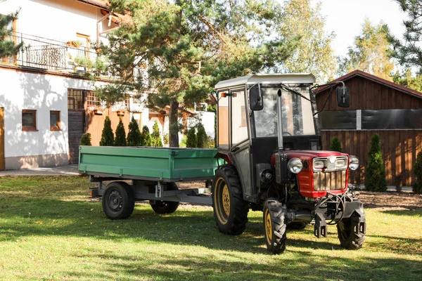 Modern tractor with empty trailer on green lawn outdoors
