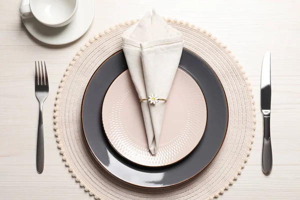 Plates with fabric napkin, decorative ring and cutlery on white wooden table, flat lay