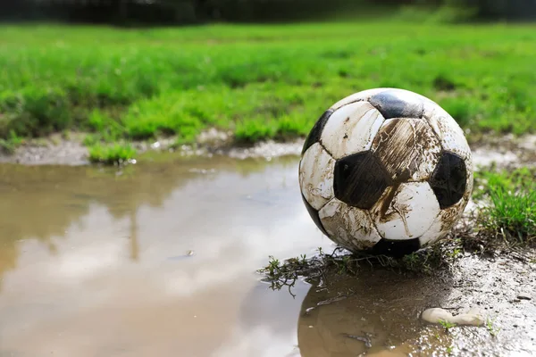 stock image Dirty soccer ball on green grass near puddle outdoors, space for text