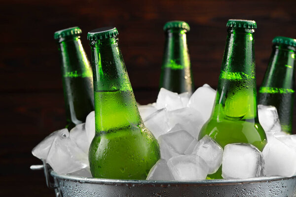 Metal bucket with bottles of beer and ice cubes on wooden background, closeup