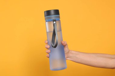 Turuncu arka planda içki şişesi tutan kadın, yakın plan.