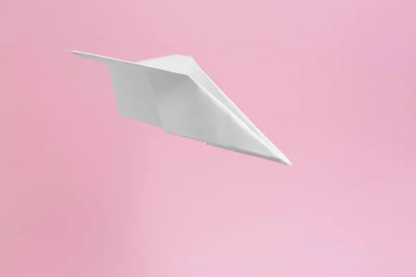 White paper plane flying on pink background, space for text